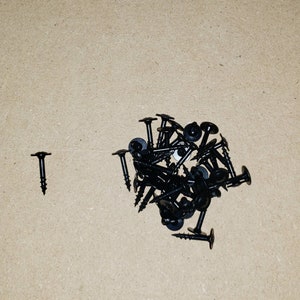 May include: A pile of black screws with a flat head and a washer on the underside. There is one screw to the left of the pile.