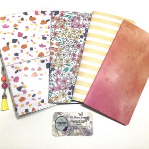 May include: A collection of TN Mama Journals, featuring various patterned covers. Designs include terrazzo, floral, striped, and watercolor effects. A small business card with the text "TN mama JOURNALS" is also present, along with a tassel charm.