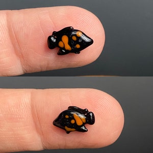 Puede incluir: Una peque&ntilde;a figurita de pez negra y naranja con un dise&ntilde;o detallado. La figurita mide aproximadamente 2,5 cm de largo y est&aacute; hecha de vidrio.