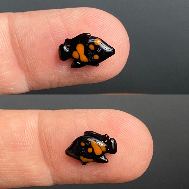 Puede incluir: Una peque&ntilde;a figurita de pez negra y naranja con un dise&ntilde;o detallado. La figurita mide aproximadamente 2,5 cm de largo y est&aacute; hecha de vidrio.