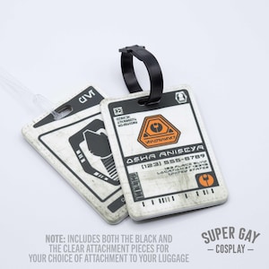 May include: Two white luggage tags with black and orange details. The tag on the left has a symbol of a person with a helmet. The tag on the right has a symbol of a person with a helmet and the text "OSHA ANISEYA (123) 555-6789 183 PLACE BLVD LOCATION 87 18345 UNITED STATES".