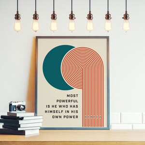Puede incluir: Impresi&oacute;n art&iacute;stica enmarcada con un c&iacute;rculo turquesa y l&iacute;neas conc&eacute;ntricas naranjas, con la cita "MOST POWERFUL IS HE WHO HAS HIMSELF IN HIS OWN POWER" de S&eacute;neca. Una c&aacute;mara vintage y una pila de libros sobre una superficie de madera.