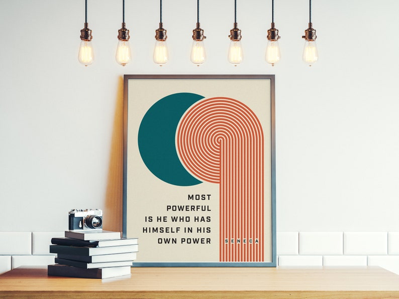 Puede incluir: Impresi&oacute;n art&iacute;stica enmarcada con un c&iacute;rculo turquesa y l&iacute;neas conc&eacute;ntricas naranjas, con la cita "MOST POWERFUL IS HE WHO HAS HIMSELF IN HIS OWN POWER" de S&eacute;neca. Una c&aacute;mara vintage y una pila de libros sobre una superficie de madera.