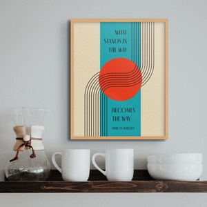 May include: A framed print with a teal background and a red circle with black lines. The text reads "What stands in the way becomes the way" - Marcus Aurelius.