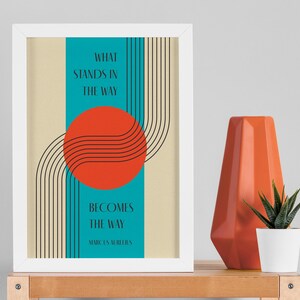 May include: A framed print with a minimalist design featuring a red circle, black lines, and a turquoise background. The text reads "What stands in the way becomes the way - Marcus Aurelius".