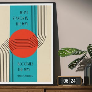 May include: A framed print with a teal blue background and a red circle with black lines. The text "What stands in the way becomes the way" is printed in black on a white background. The quote is attributed to Marcus Aurelius.