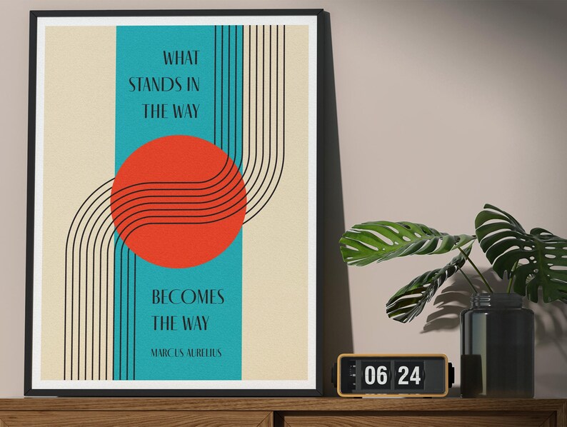 May include: A framed print with a teal blue background and a red circle with black lines. The text "What stands in the way becomes the way" is printed in black on a white background. The quote is attributed to Marcus Aurelius.