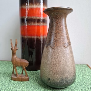 May include: A still life arrangement featuring two ceramic vases and a wooden deer sculpture. The taller vase has brown, orange, and white bands. The other vase is a speckled brown. The deer figurine is made of wood.