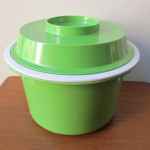 May include: A green plastic ice bucket with a white rim and a lid. The lid has a small, round indentation in the centre.