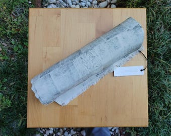 May include: A rolled up piece of white fabric with a gray print on a light wood surface. A small white tag with black text is attached to the fabric.