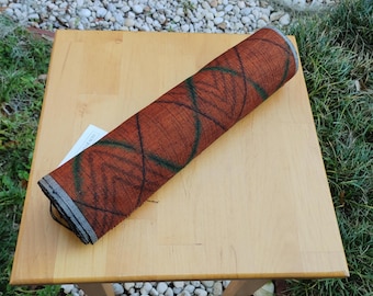 May include: A rolled up brown and green fabric with a geometric pattern. The fabric is on a wooden table.
