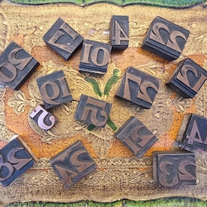May include: A collection of rectangular wooden letterpress blocks featuring raised metal numbers including 2, 4, 7, 10, 12, 14, 15, 19, 20, 22, 23, 24, 25, and 27. Each block has a dark wooden base with a metallic, copper-toned number relief on the top surface.
