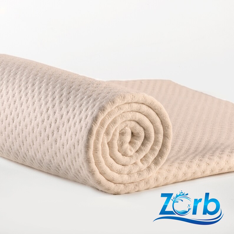 May include: A rolled up beige waffle weave towel with a textured surface. The towel is rolled up tightly and is lying on a white surface.