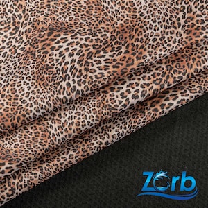 May include: Brown and black leopard print fabric with a subtle sheen. The fabric is folded in thirds and the bottom edge is resting on a black surface.