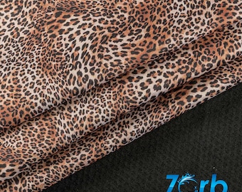 Puede incluir: Tela de estampado de leopardo marrón y negro con un brillo sutil. La tela está doblada en tres partes y el borde inferior descansa sobre una superficie negra.