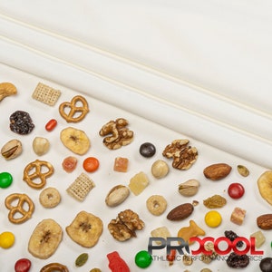 May include: A white fabric background with a variety of snacks scattered across the surface. The snacks include pretzels, nuts, dried fruit, cereal, and candy. The text "PROCOOL ATHLETIC PERFORMANCE FABRICS" is visible in the bottom right corner of the image.
