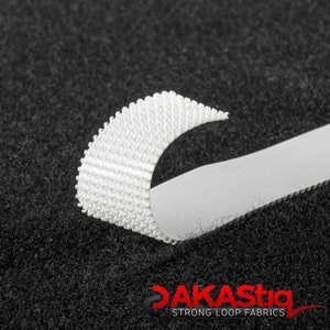 May include: Close-up of white hook and loop fastener tape. The tape is made of a soft, flexible material and has a textured surface. The tape is attached to a black fabric background.