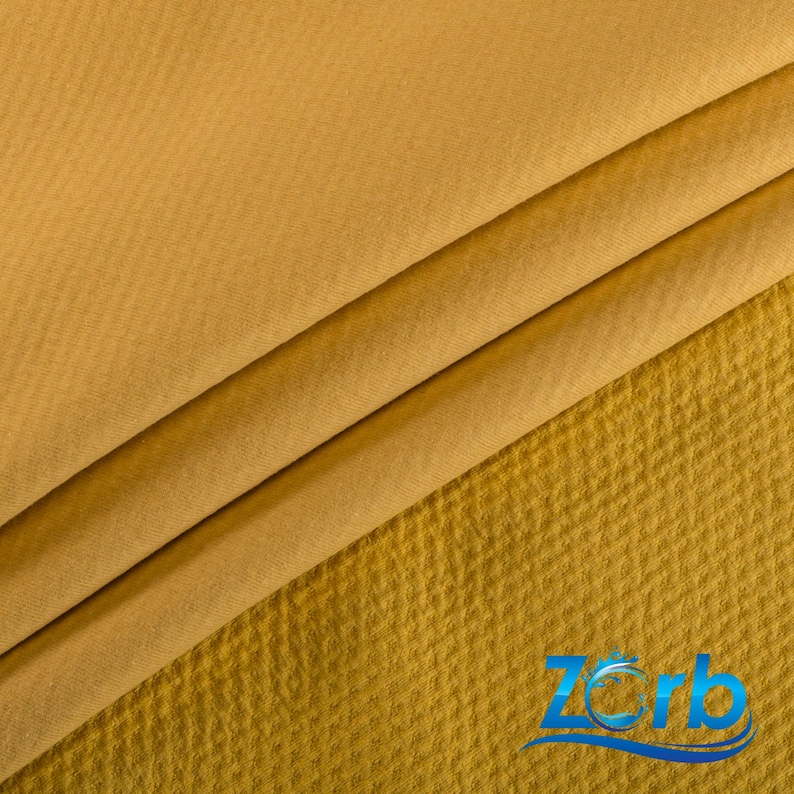 May include: Close-up of a mustard yellow fabric with a textured waffle weave. The fabric is folded in thirds, showing the texture of the material.