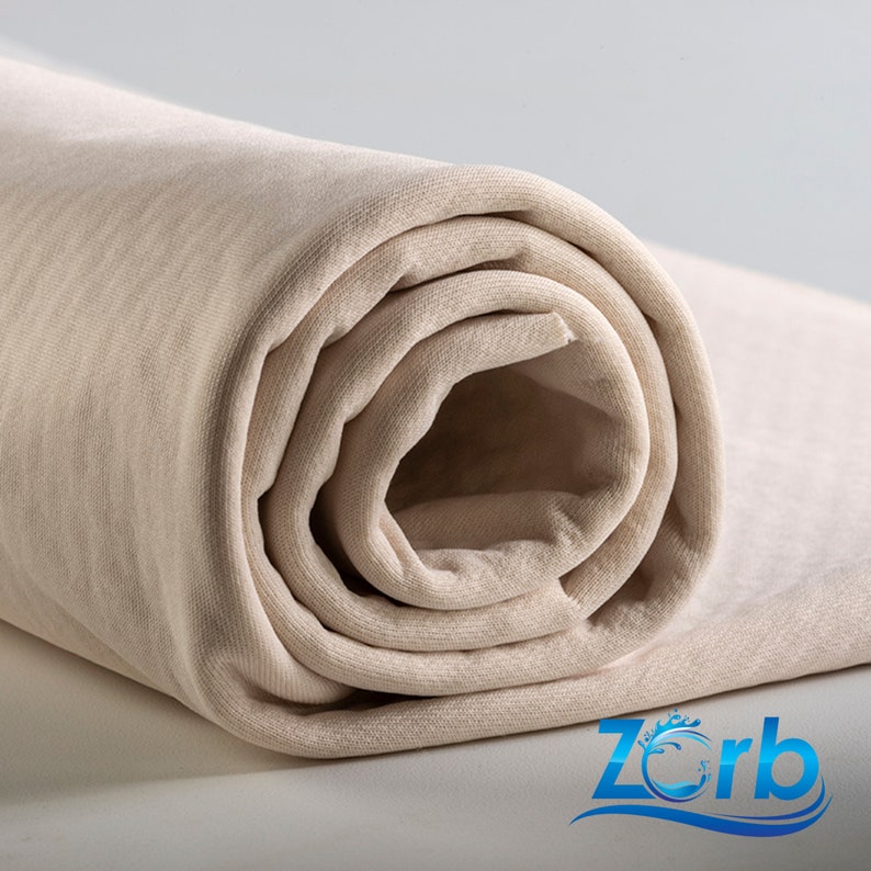 Puede incluir: Primer plano de una tela beige enrollada. La tela es suave y tiene una superficie ligeramente texturizada.