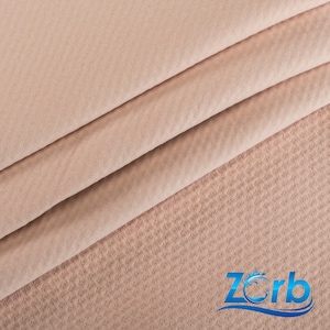 May include: Close-up of a light brown fabric with a textured pattern. The fabric is folded in thirds, with the top layer folded over the bottom two layers. The fabric is soft and smooth to the touch.