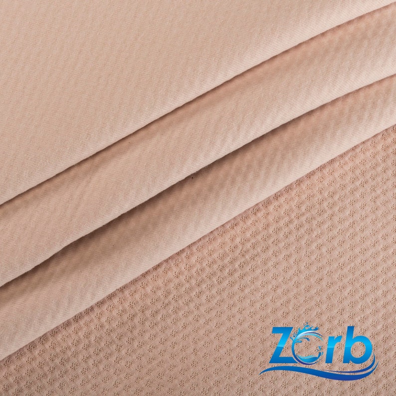 May include: Close-up of a light brown fabric with a textured pattern. The fabric is folded in thirds, with the top layer folded over the bottom two layers. The fabric is soft and smooth to the touch.