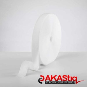May include: A white roll of hook and loop tape, also known as Velcro, is shown on a white surface. The tape is rolled up and a portion of the tape is unrolled, showing the soft, fuzzy texture of the loop side.