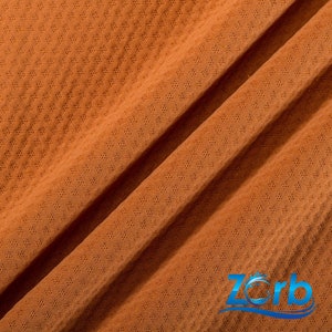 Puede incluir: Primer plano de una tela marr&oacute;n texturizada con un patr&oacute;n de diamante. La tela est&aacute; doblada por la mitad, creando una l&iacute;nea diagonal. La tela es suave y transpirable, lo que la hace ideal para ropa deportiva o ropa casual.