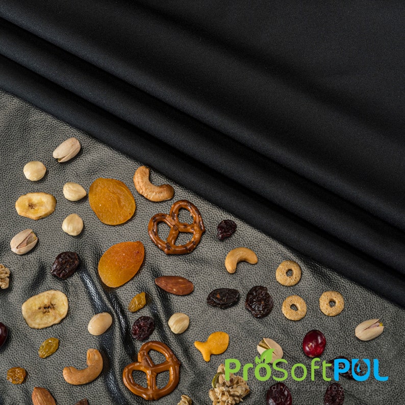 May include: A variety of snacks, including pretzels, dried fruit, nuts, and cereal, are scattered on a silver surface. The snacks are arranged in a semi-circle shape, with a black fabric background.