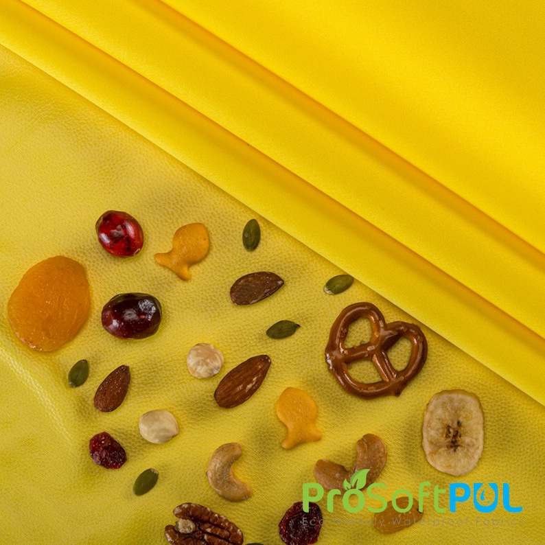 May include: A yellow surface with a variety of snacks, including pretzels, dried fruit, nuts, and pumpkin seeds. The snacks are arranged in a random pattern.