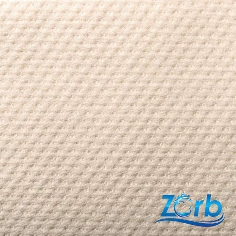 May include: Close-up of a white, textured fabric with a subtle pattern. The fabric has a soft, quilted appearance.