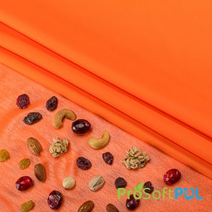 May include: A close-up of a variety of nuts and dried cranberries scattered on an orange fabric background. The nuts include cashews, almonds, and walnuts. The cranberries are a deep red color.