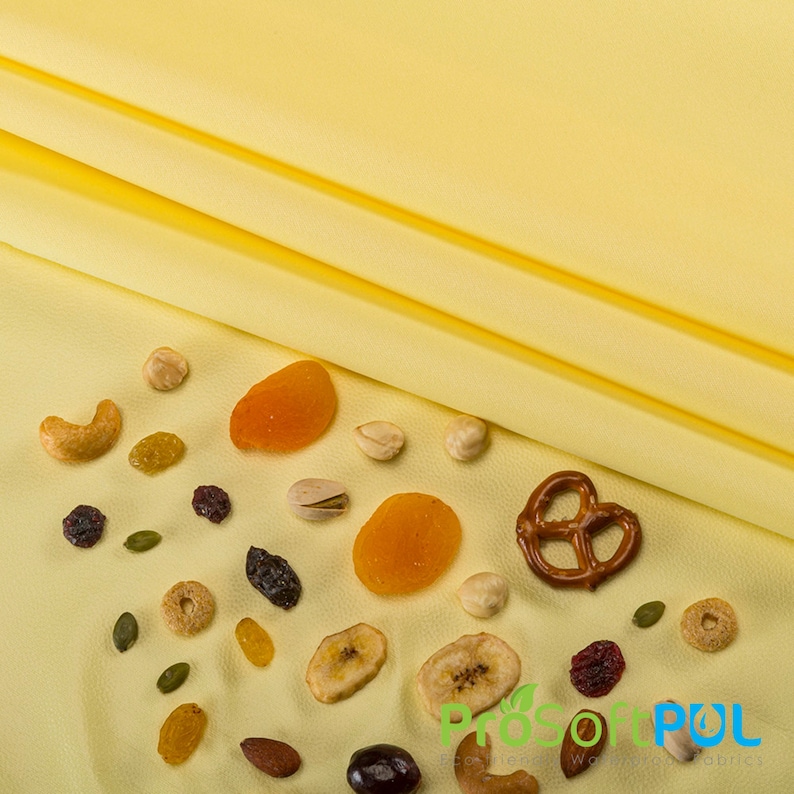 May include: A yellow surface with a variety of dried fruits, nuts, and pretzels scattered across it. The items include dried apricots, banana chips, cashews, hazelnuts, pistachios, pumpkin seeds, raisins, and pretzels.