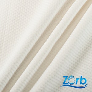 Puede incluir: Primer plano de una tela blanca texturizada con un patr&oacute;n sutil. La tela est&aacute; doblada en dos lugares, creando una l&iacute;nea diagonal. La tela es suave y lisa al tacto. La tela es un material de alta calidad que es perfecto para una variedad de proyectos.