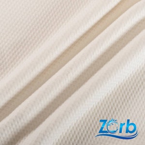 Puede incluir: Primer plano de una tela blanca con textura de gofre con un logotipo azul y blanco que dice "Zorb" en la esquina inferior derecha.