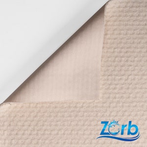 Puede incluir: Primer plano de una tela beige con textura de gofre y un respaldo blanco. La tela est&aacute; doblada para mostrar el respaldo blanco. La tela tiene un patr&oacute;n sutil y una sensaci&oacute;n suave y mullida. La tela est&aacute; etiquetada con "Zorb" en texto azul con un dise&ntilde;o de onda estilizado.