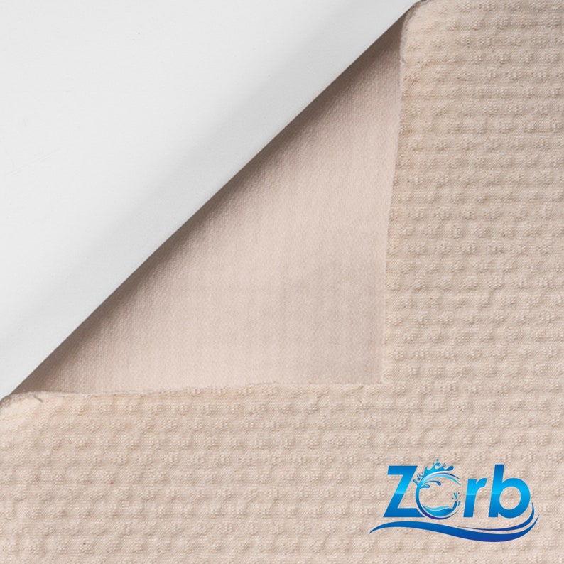 Puede incluir: Primer plano de una tela beige con textura de gofre y un respaldo blanco. La tela est&aacute; doblada para mostrar el respaldo blanco. La tela tiene un patr&oacute;n sutil y una sensaci&oacute;n suave y mullida. La tela est&aacute; etiquetada con "Zorb" en texto azul con un dise&ntilde;o de onda estilizado.