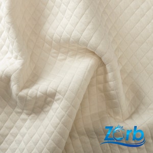 May include: Close-up of a white quilted fabric with a diamond pattern. The fabric is soft and textured, and it has a subtle sheen.