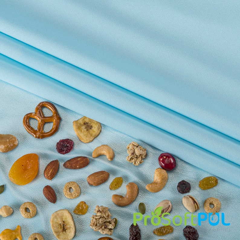 May include: A blue fabric background with a variety of nuts, dried fruit, and pretzels scattered on the surface. The nuts include almonds, cashews, and pistachios. The dried fruit includes apricots and cranberries. The pretzels are in the shape of a pretzel.