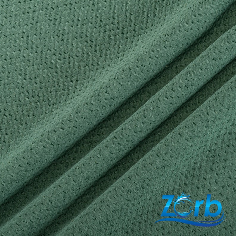 Puede incluir: Primer plano de una tela verde texturizada con un sutil patr&oacute;n de diamante. La tela es suave y tiene un ligero brillo.