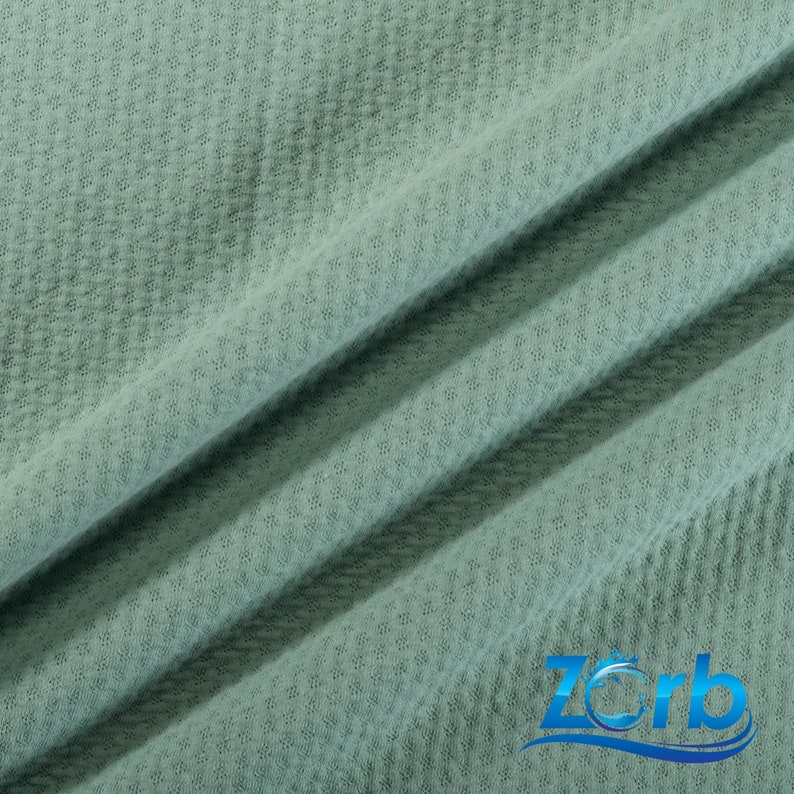 May include: A close-up of a soft, textured, sage green fabric. The fabric has a waffle-like texture and is folded in a few places.
