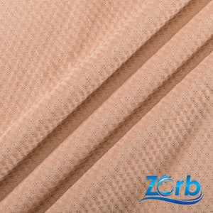 Puede incluir: Primer plano de una tela beige con un patr&oacute;n texturizado tipo gofre. La tela est&aacute; doblada en diagonal, creando un aspecto suave y drapeado.