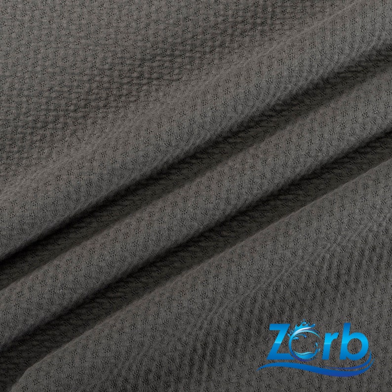 May include: Close-up of a dark gray textured fabric with a subtle waffle pattern. The fabric is folded in a diagonal pattern, creating a soft and inviting look.