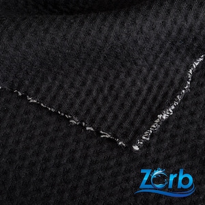 May include: Close-up of a black fabric with a textured surface. The fabric has a raw edge with white stitching.