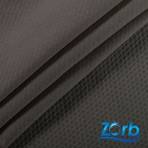 May include: Close-up of a dark gray fabric with a textured waffle weave pattern. The fabric is folded in thirds, revealing the underside of the fabric. The fabric is labeled with the word "Zorb" in a blue and white logo.