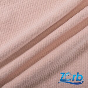 May include: A close-up of a soft, pink waffle knit fabric. The fabric has a textured surface and is folded in a few places.