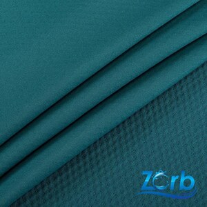 May include: Close-up of teal fabric with a smooth, draped texture. The fabric is folded, revealing subtle shadows and highlights. A section of textured, diamond-patterned fabric is visible, adding contrast. The overall aesthetic suggests textiles for clothing or home decor.