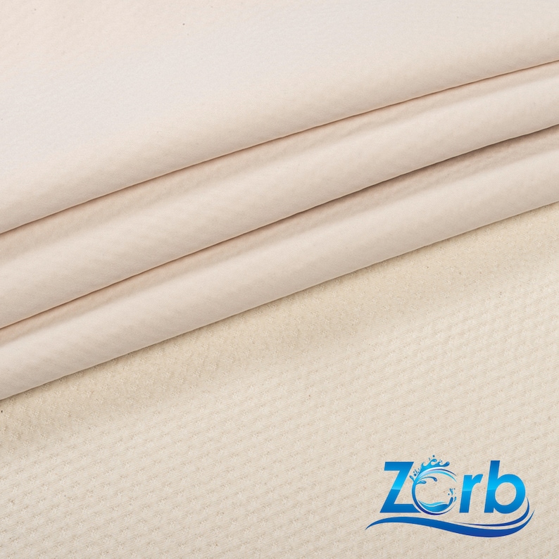 May include: Close-up of a white fabric with a textured surface. The fabric is folded in thirds and the bottom layer is slightly visible. The fabric is labeled "Zorb" in blue text with a stylized wave design.
