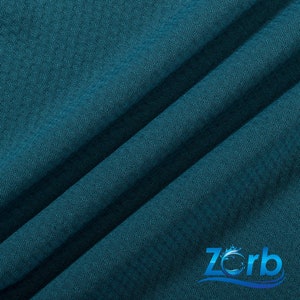 Puede incluir: Primer plano de una tela azul turquesa con tejido texturizado. La tela est&aacute; doblada en diagonal. La palabra "Zorb" es visible en la esquina inferior derecha de la imagen.