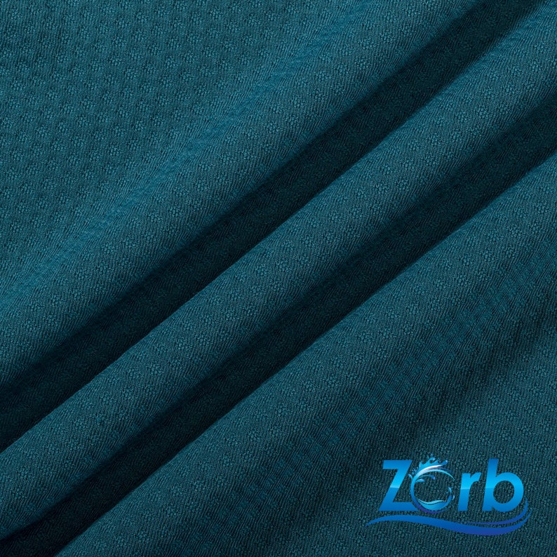 Puede incluir: Primer plano de una tela azul turquesa con tejido texturizado. La tela est&aacute; doblada en diagonal. La palabra "Zorb" es visible en la esquina inferior derecha de la imagen.