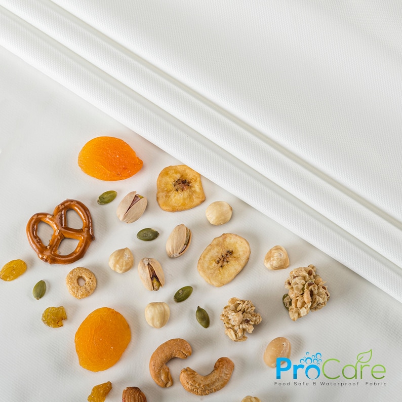 May include: A white fabric with the text "ProCare Food Safe & Waterproof Fabric" on a white background with a variety of snacks scattered on the fabric, including pretzels, dried fruit, nuts, and granola.